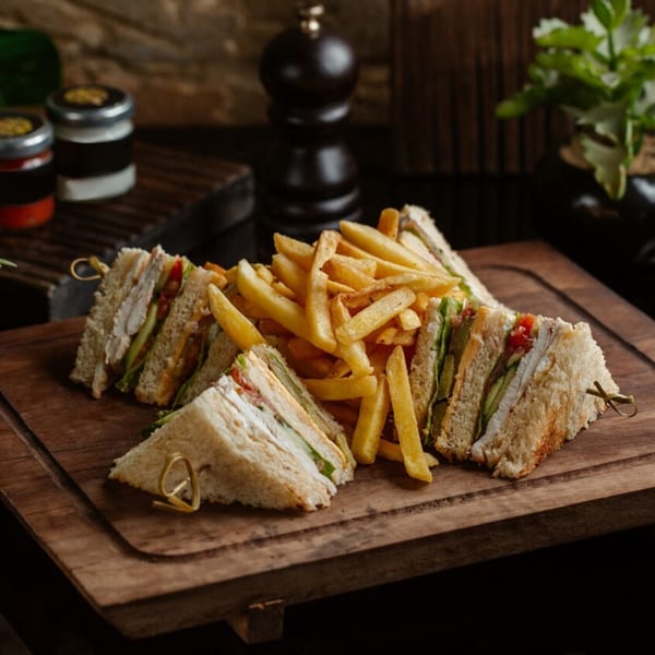 Club sandwiches with chicken, lettuce, and tomato, served with golden french fries on a wooden board.
