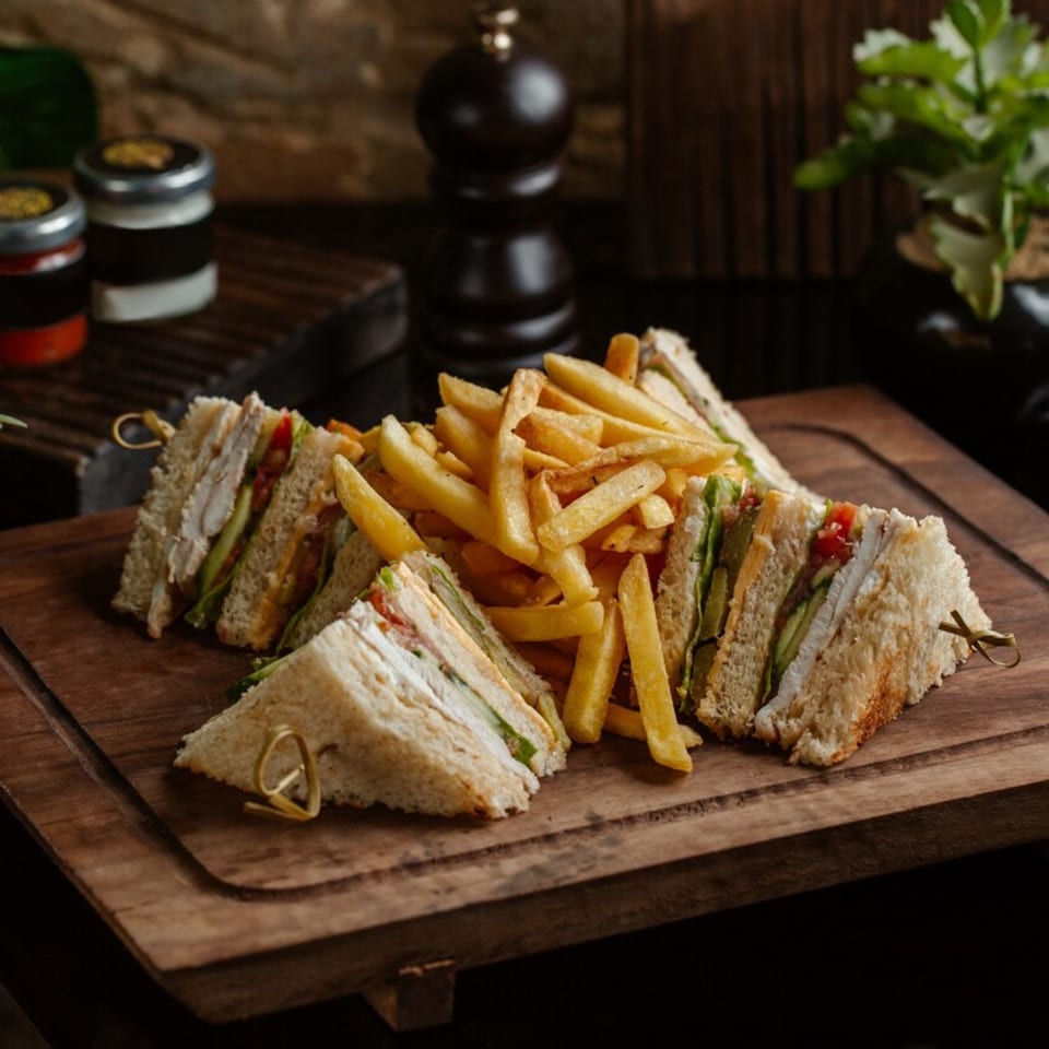 Club sandwiches with chicken, lettuce, and tomato, served with golden french fries on a wooden board.