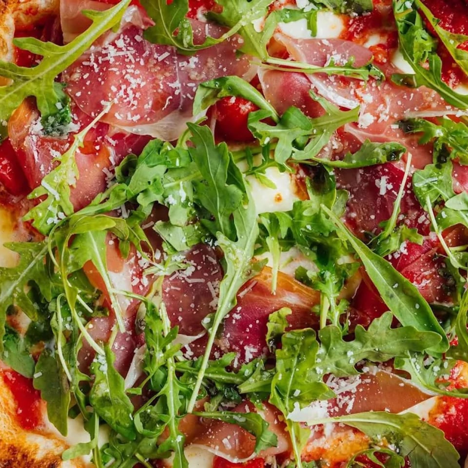 Close-up of a pizza topped with prosciutto, fresh arugula, and grated cheese.
